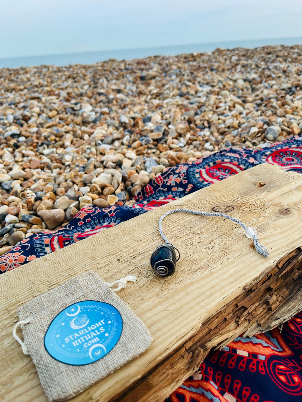 Blue Quartz spiral pendulum wrapped in titanium wire, displayed alongside other handcrafted crystal pendulums against a bright blue sky.