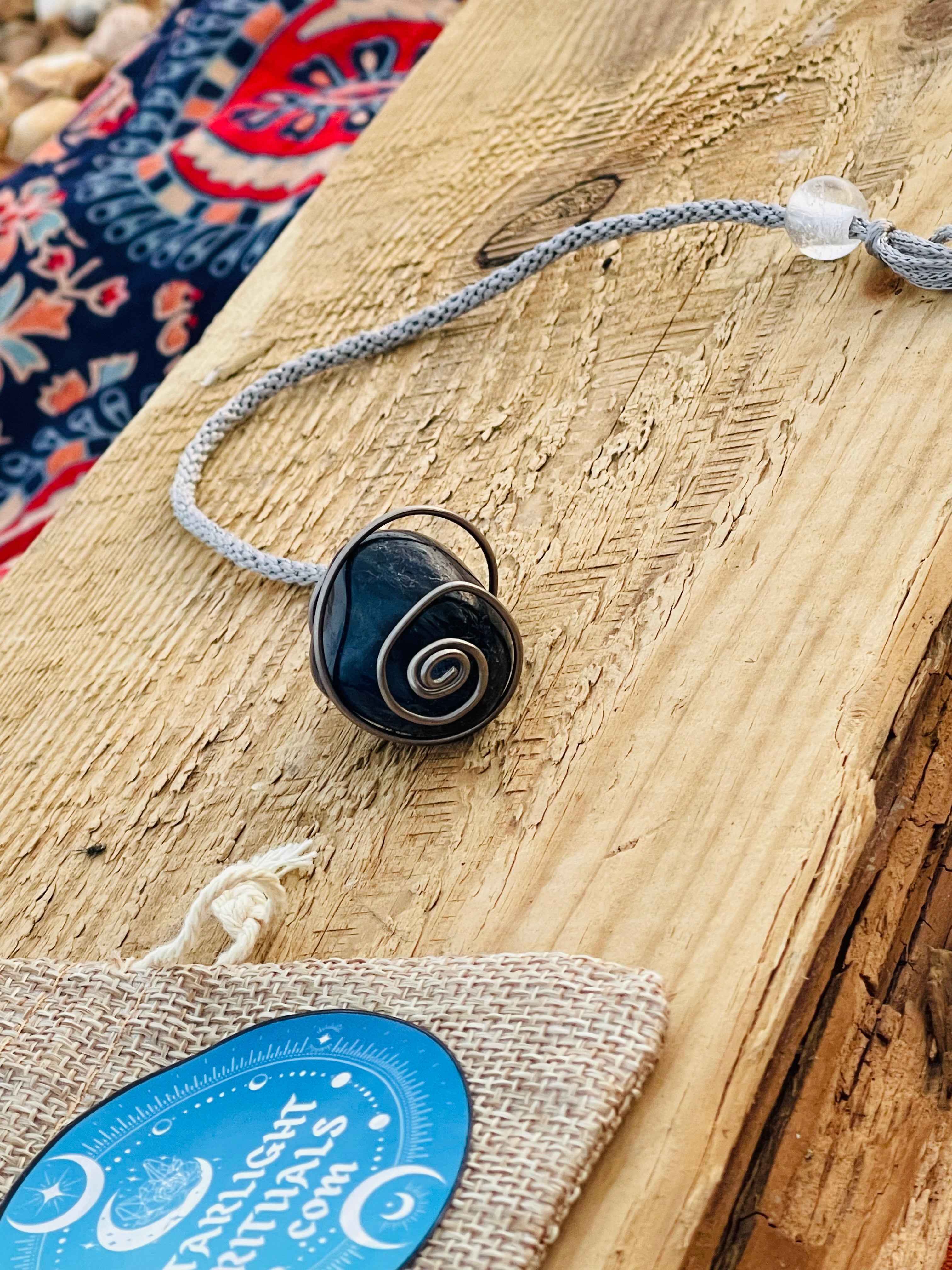 Handcrafted Blue Quartz spiral pendulum wrapped in titanium wire, displayed on rustic wood with an adjustable grey cord, natural cotton gift pouch and Starlight Rituals tag.