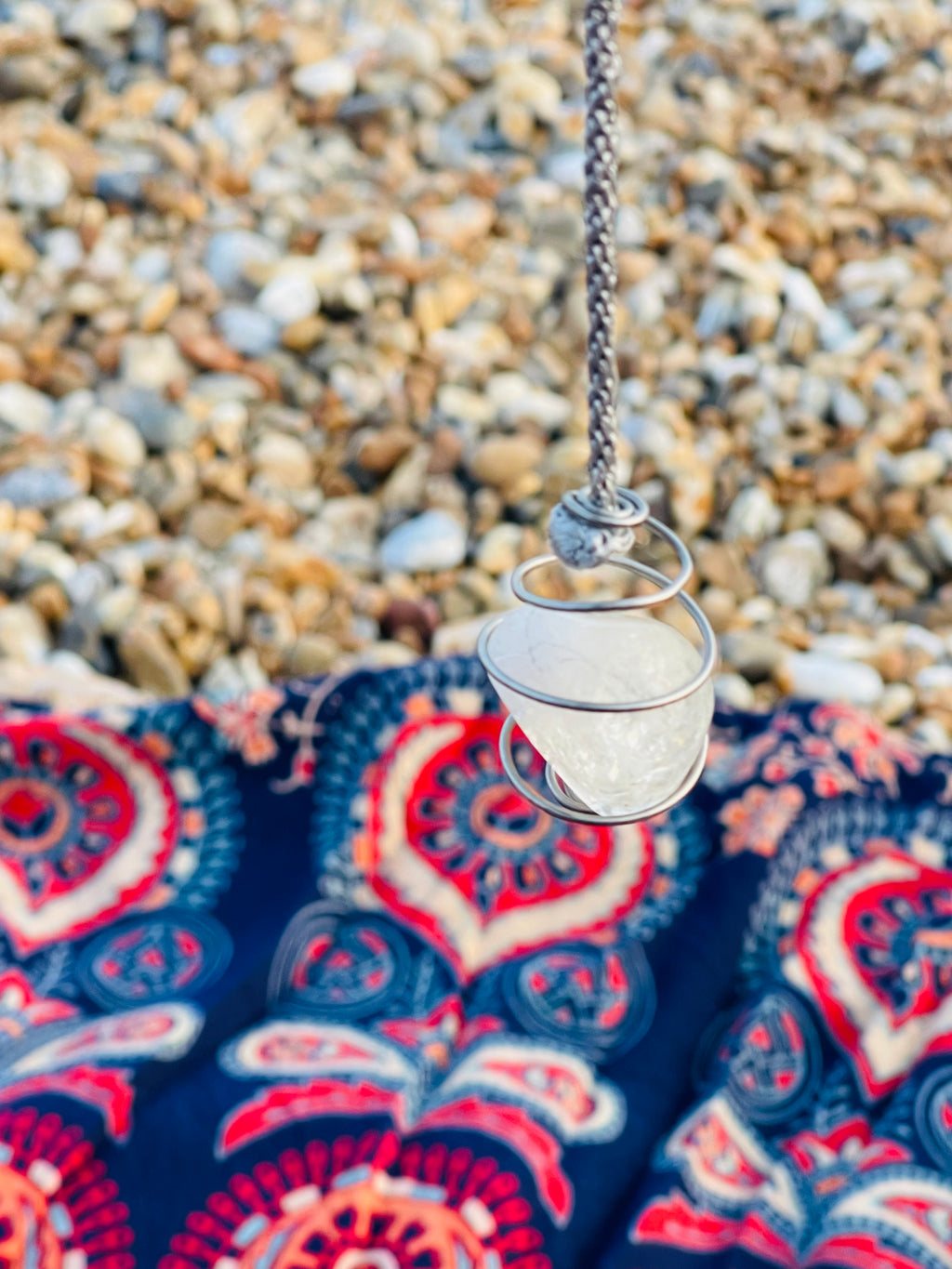 Handcrafted natural Citrine crystal pendulum wrapped in Grade 1 titanium wire, suspended from a hand braided rayon cord above a patterned blanket on a Kent pebble beach.