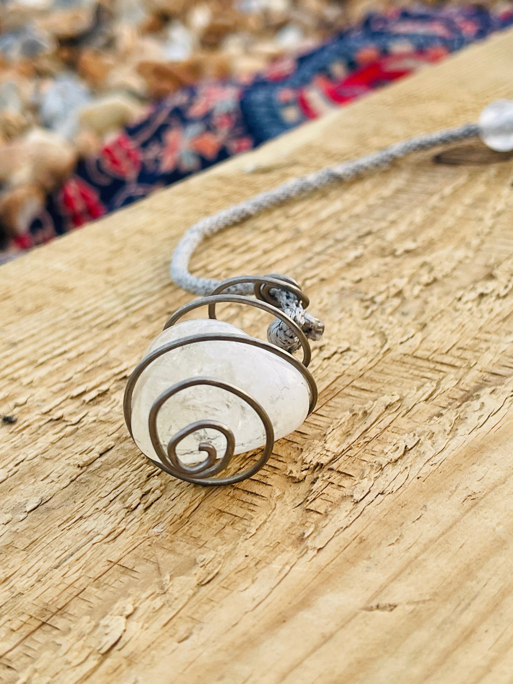 Side view of a handcrafted natural Citrine crystal pendulum wrapped in Grade 1 titanium wire, resting on rustic driftwood and highlighting the spiral wire craftsmanship.