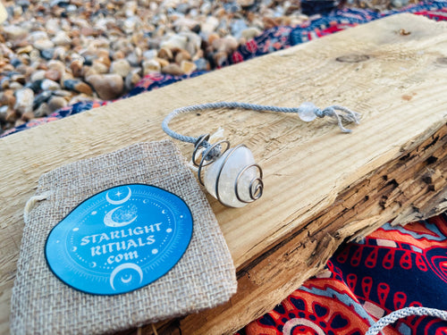 Handcrafted natural Citrine crystal pendulum wrapped in Grade 1 titanium wire, displayed with a Starlight Rituals linen gift pouch on rustic driftwood beside a pebble beach on the Kent coast.