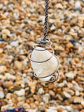 Handcrafted Citrine crystal pendulum wrapped in Grade 1 titanium wire, suspended from a hand braided rayon cord above a pebble beach on the Kent coast.