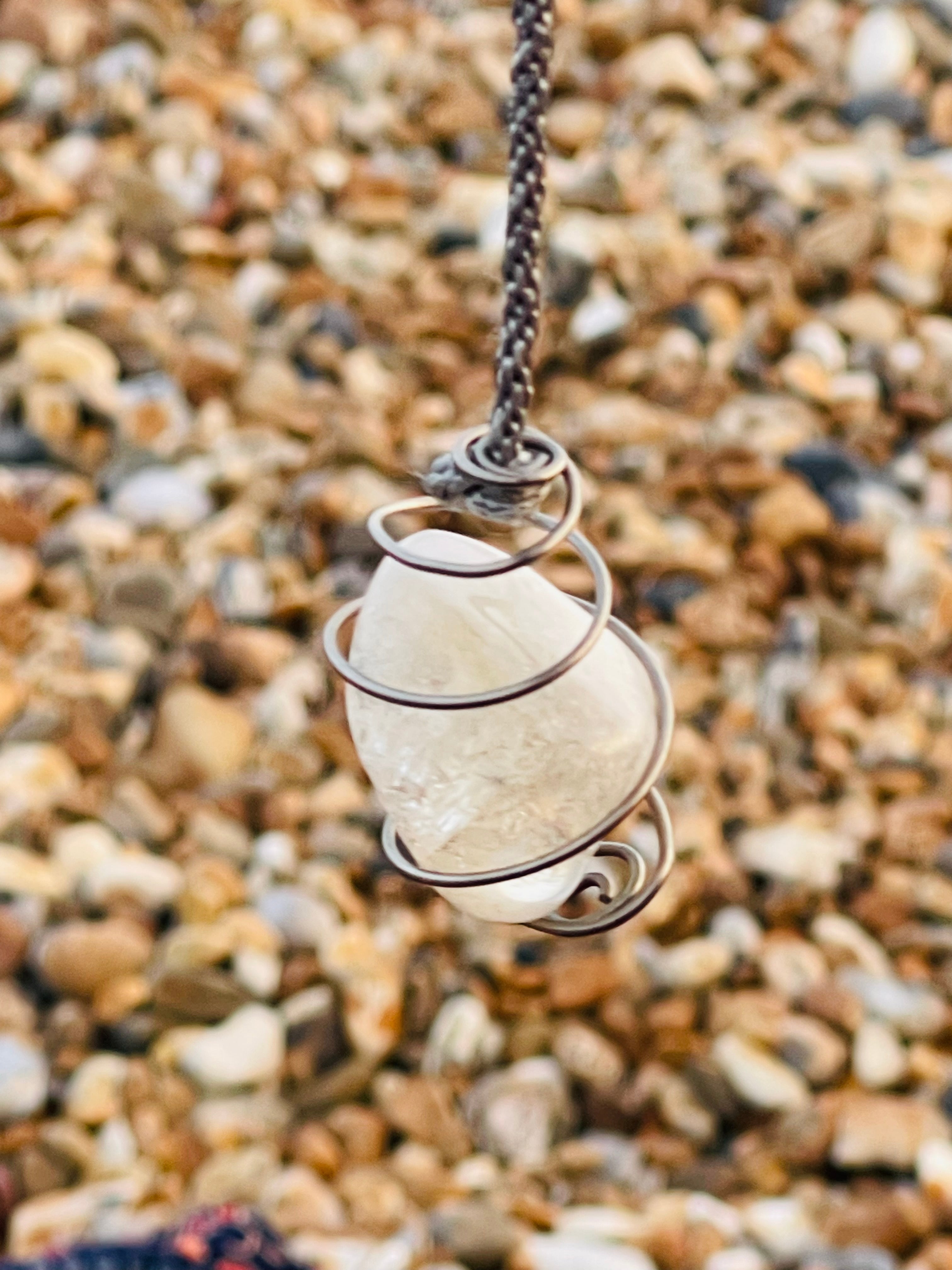 Handcrafted Citrine crystal pendulum wrapped in Grade 1 titanium wire, suspended from a hand braided rayon cord above a pebble beach on the Kent coast.