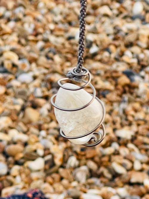 Handcrafted Citrine crystal pendulum wrapped in Grade 1 titanium wire, suspended from a hand braided rayon cord above a pebble beach on the Kent coast.