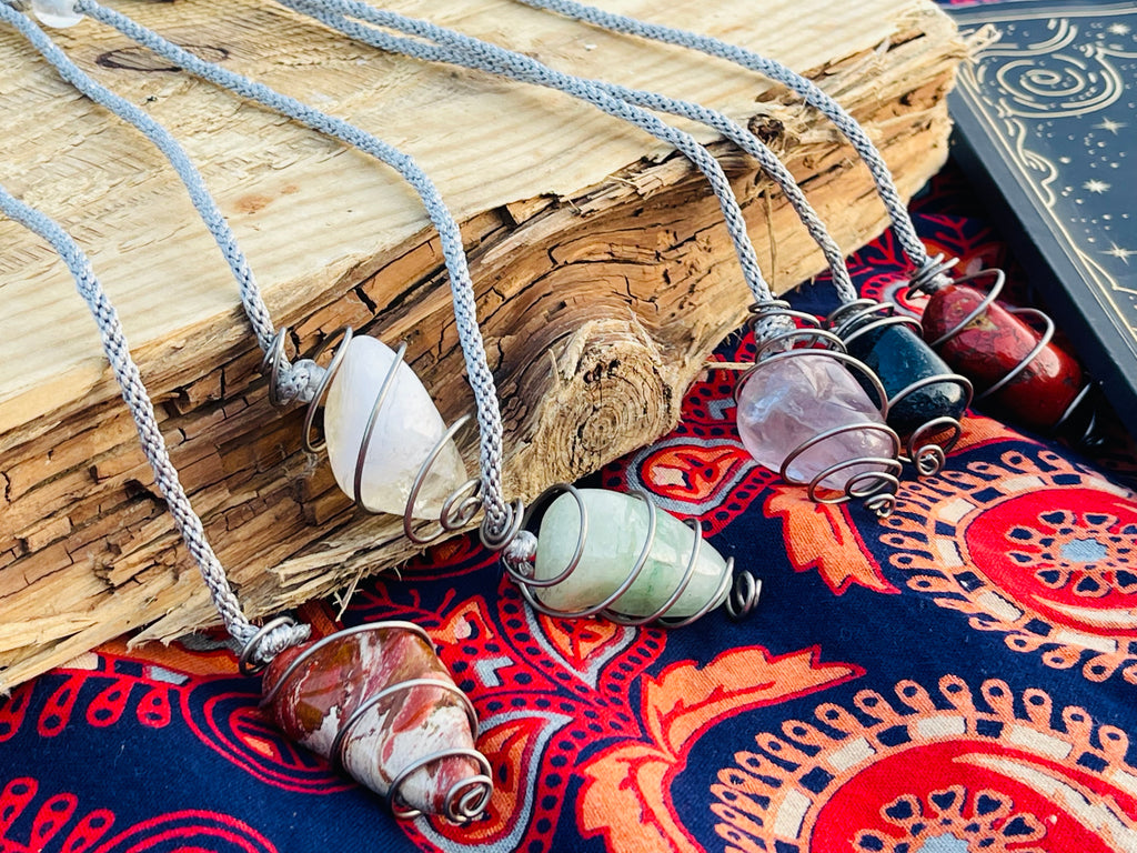 Selection of handcrafted Starlight Rituals crystal pendulums displayed on driftwood with hand-braided rayon cords and natural gemstones.