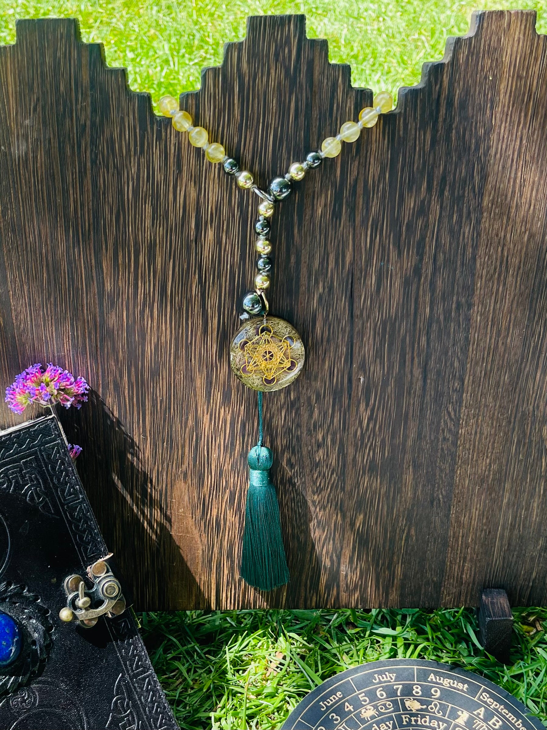 Path of Prosperity 108-bead crystal mala displayed on a wooden stand, featuring a Metatron's Cube talisman and emerald green tassel for meditation and mindful practice.