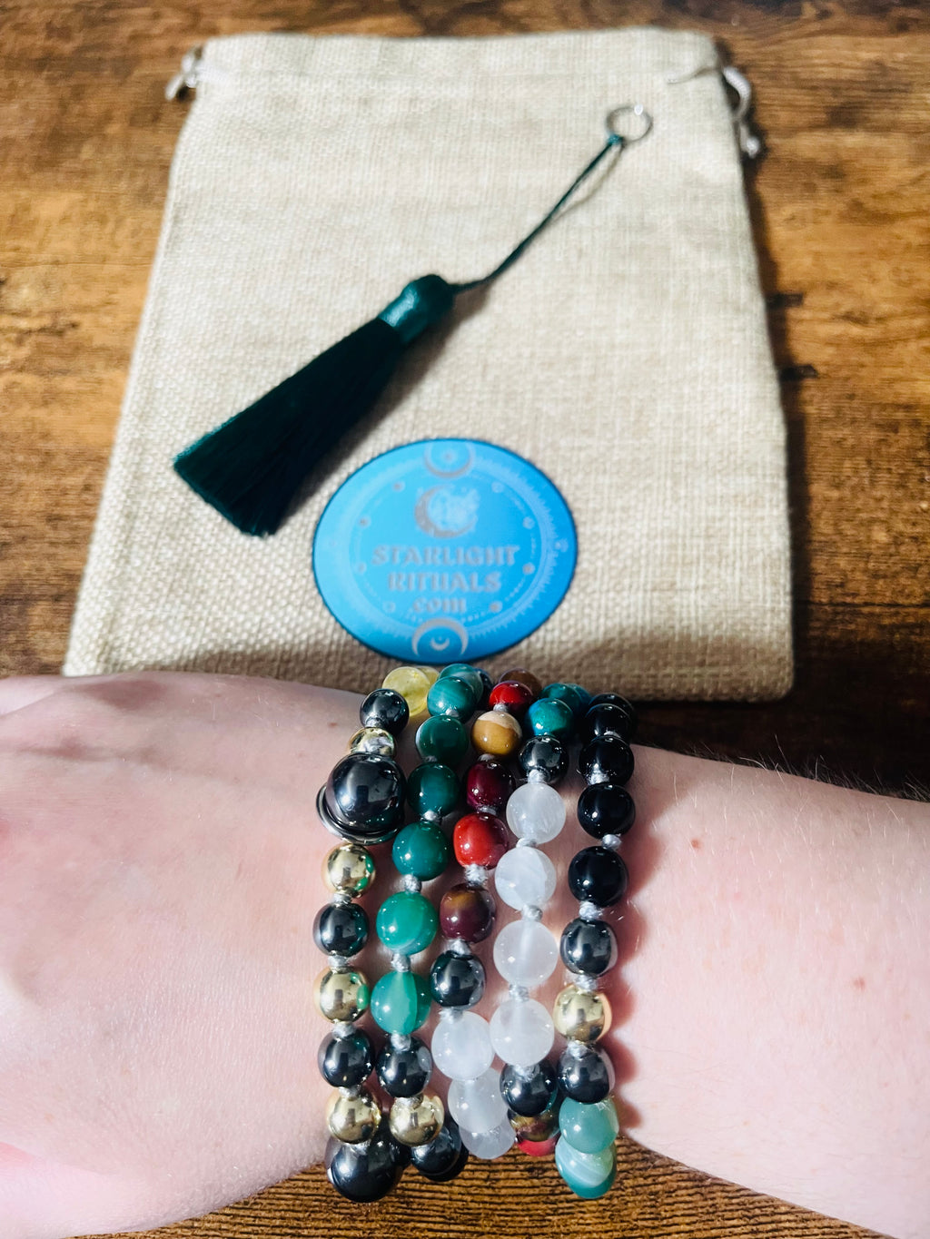 Path of Prosperity 108-bead crystal mala wrapped and worn as a bracelet, with the removable emerald green tassel and Starlight Rituals gift pouch shown behind.
