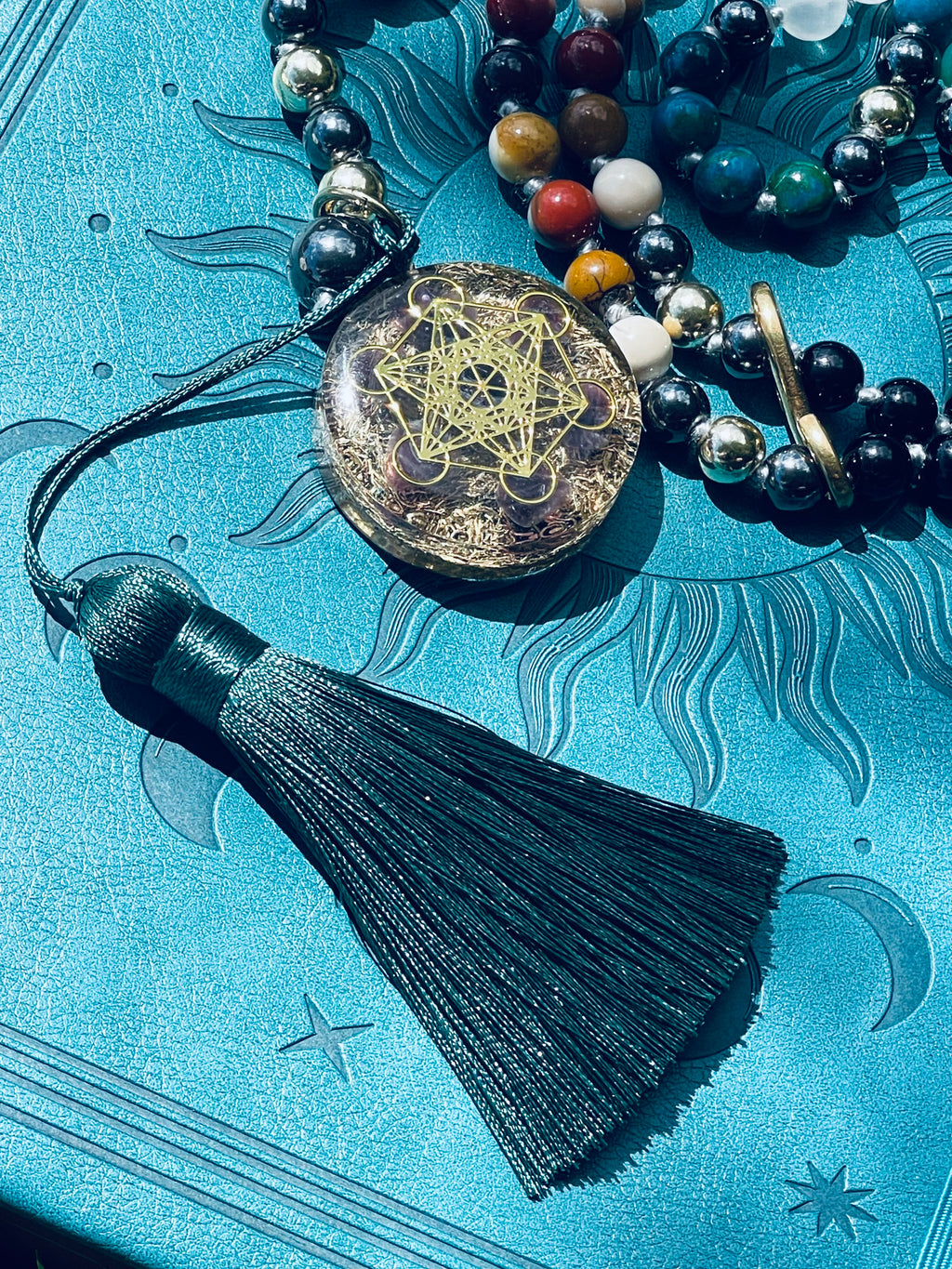 Close-up detail of the Path of Prosperity crystal mala showing the Metatron's Cube talisman, emerald green tassel and hand-knotted gemstone beads.