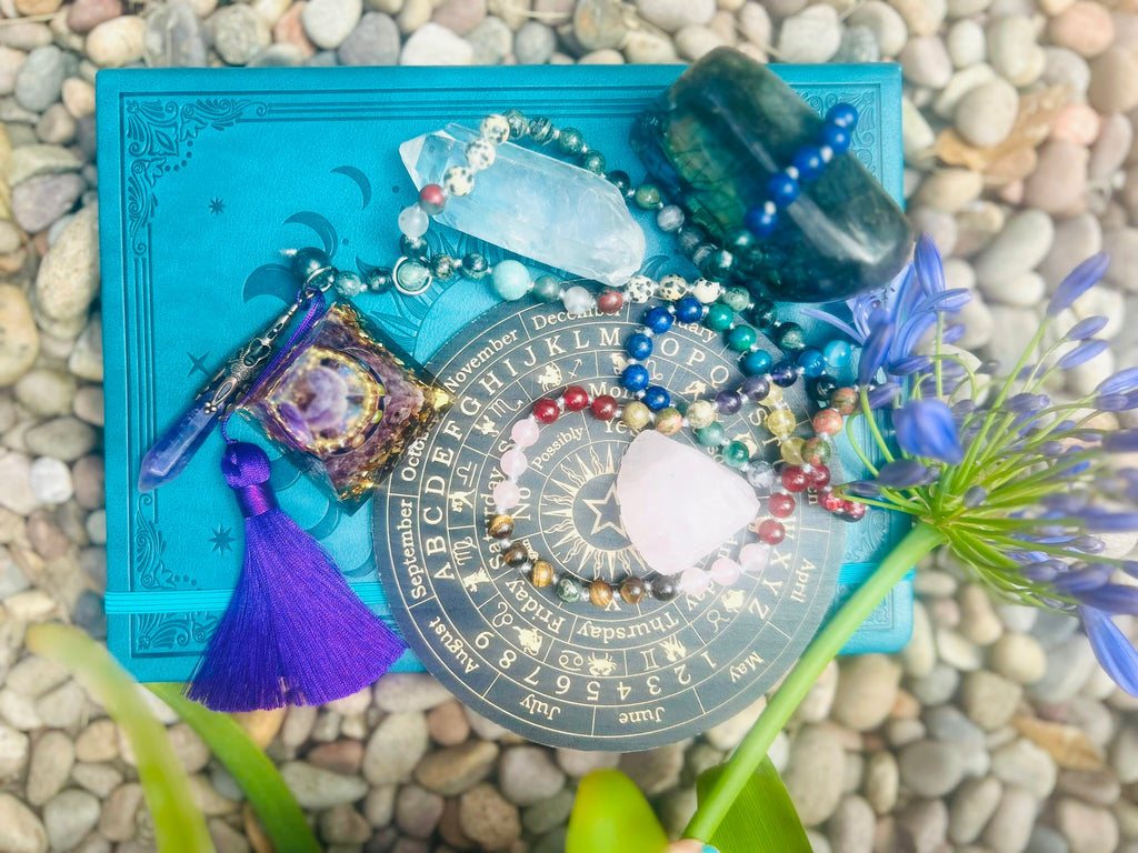Handcrafted bespoke crystal mala by Starlight Rituals displayed alongside a crystal journal, natural crystals and botanical elements as part of a peaceful ritual-inspired flat lay.