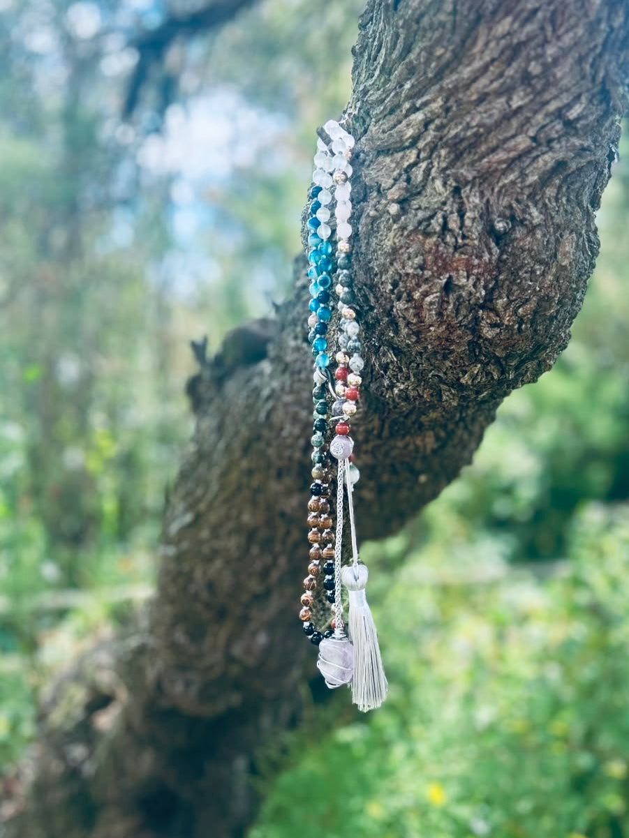 Handcrafted bespoke crystal mala by Starlight Rituals displayed on a tree branch in a peaceful natural setting, showcasing the elegant drape and natural gemstones.