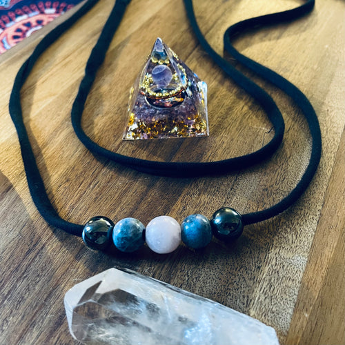 Handmade Crystal Comfort Belt with five hematine, sodalite and rose quartz beads threaded onto soft black bamboo jersey, displayed on a wooden surface with crystals.