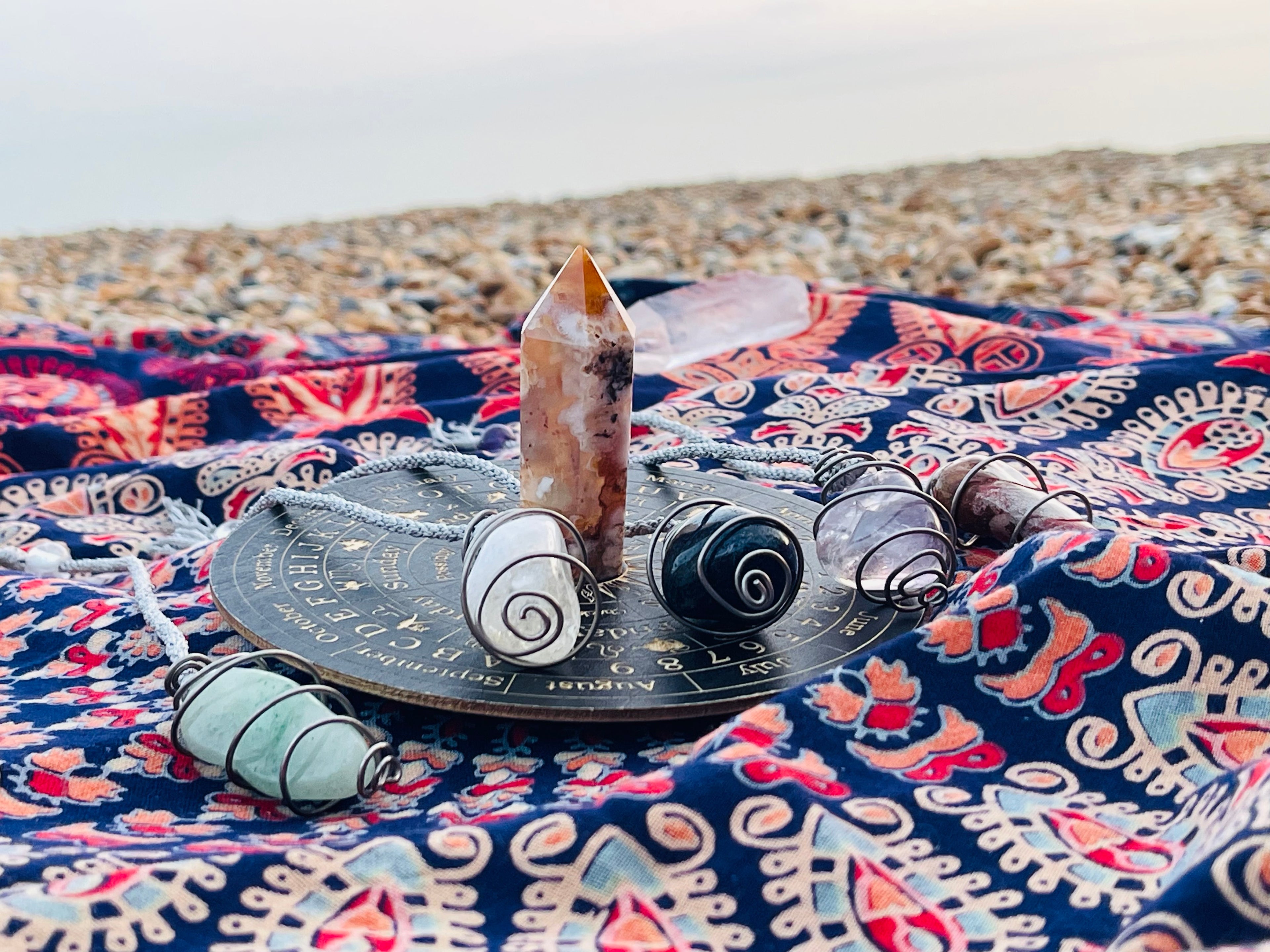 Handcrafted Starlight Rituals crystal pendulum collection displayed with ritual tools on a pebble beach on the Kent coast.