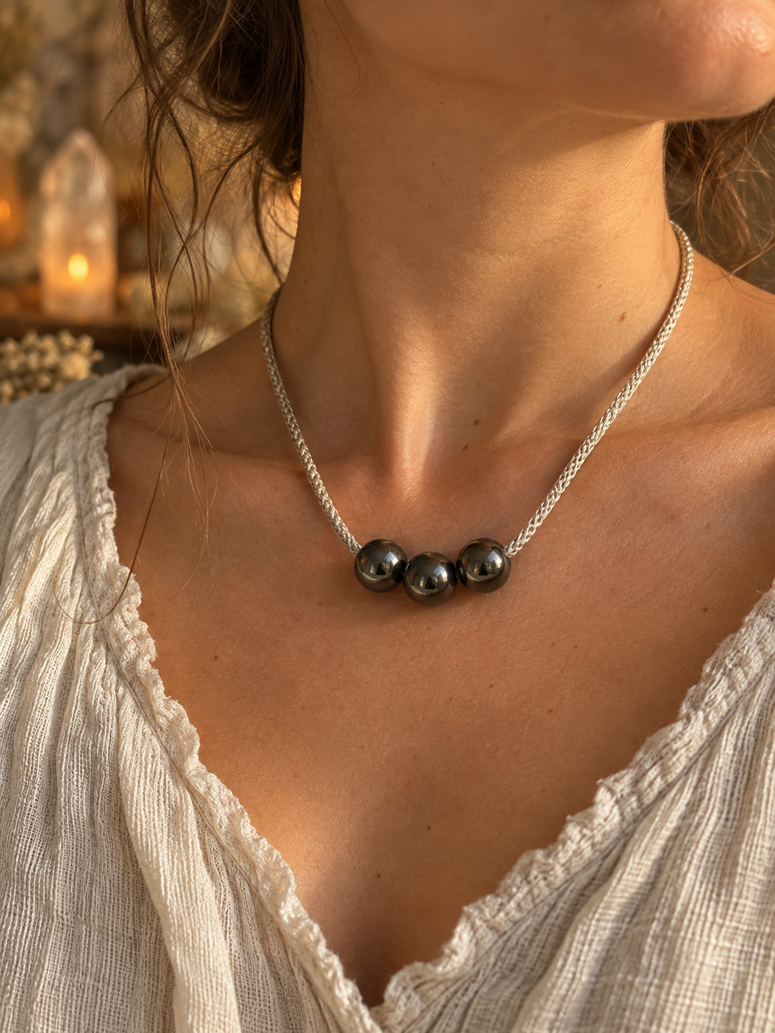 Starlight Rituals handmade necklace featuring three polished metallic hematine beads on a silver hand-braided cord, worn around the neck with a cream linen top