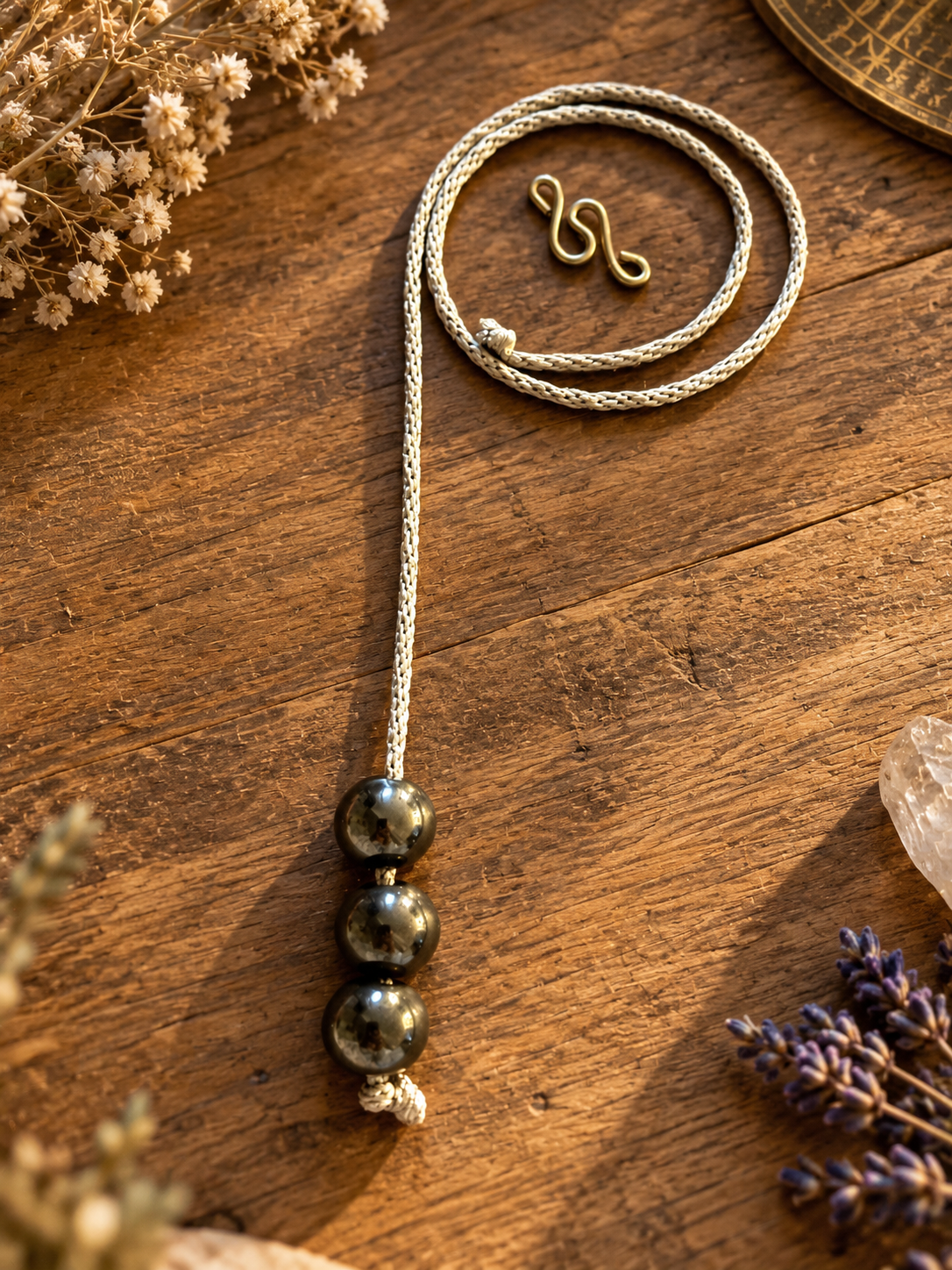 Handcrafted Starlight Rituals necklace featuring three polished metallic hematine beads on a silver hand-braided cord, displayed on rustic wood with lavender and crystals.