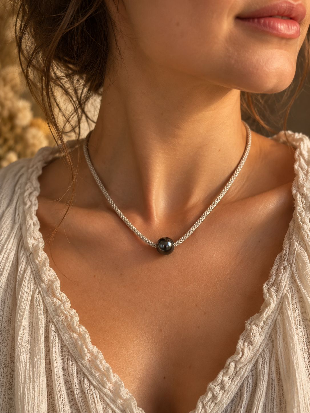 Starlight Rituals handmade necklace featuring a single polished hematine bead on a delicate silver hand-braided cord, worn at the collarbone with a cream textured top.